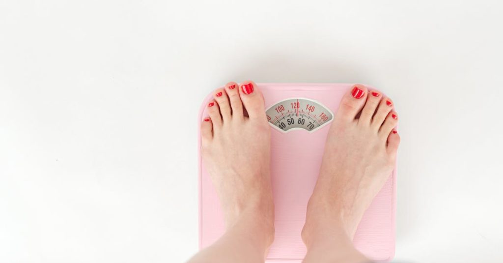 why am i gaining weight? Top view of crop anonymous barefoot female measuring weight on scales on white background